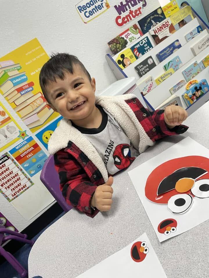 A smiling toddler giving a thumbs up after an art project